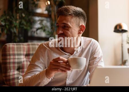 Portrait von lächelnd gut aussehenden Kerl genießen Tee während der Arbeit mit Laptop im Café. Lifestyle-Konzept Stockfoto
