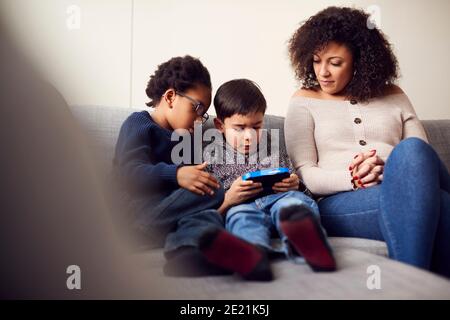 Mutter Und Söhne Sitzen Auf Sofa Zu Hause Spielen Computer Spiel Zusammen Auf Hand Held Gerät Zu Hause Stockfoto