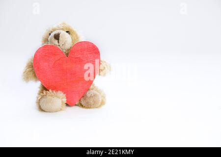 Teddybär hält ein hölzernes Herz vor weißem Hintergrund. Liebeskonzept. Stockfoto