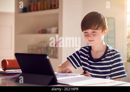 Junge Sitzt Am Küchentisch Tun Hausarbeit Mit Digital Tablet Stockfoto