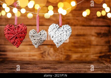 Drei handliche handgefertigte Herzen hängen auf Holzhintergrund mit Bokeh. Valentinstag Hintergrund. Speicherplatz kopieren Stockfoto