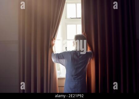 Ältere Frau Im Schlafzimmer Opening Vorhänge Am Morgen Stockfoto