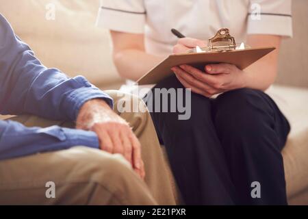 Nahaufnahme Von Weiblichen Arzt Macht Notizen Während Zu Hause Besuch Zum Senior Man Für Medizinische Prüfung Stockfoto