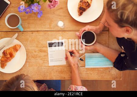 Zwei Freundinnen Im Coffee Shop Verwenden Hand Sanitizer Und Füllen Sie Das Test- Und Trace-Formular In Pandemie Aus Stockfoto