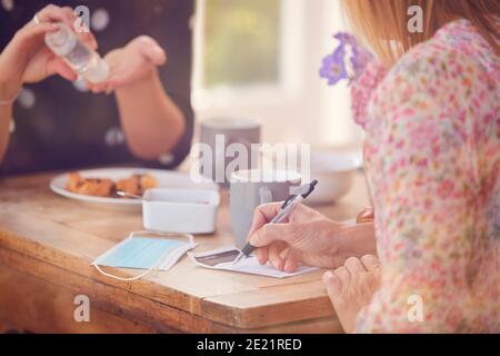 Zwei Freundinnen Im Coffee Shop Verwenden Hand Sanitizer Und Füllen Sie Das Test- Und Trace-Formular In Pandemie Aus Stockfoto