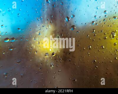 Regen fällt auf ein Fenster mit einem abstrakten Gelb und Blauer Hintergrund Stockfoto