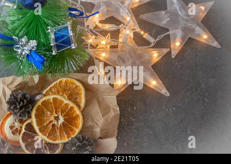 Weihnachtskomposition mit Tannenzweigen, Tannenzapfen, getrockneten Orangen und einer Girlande von Sternen auf einem dunklen Tisch. Selektiver Fokus, festliche Stimmung. Stockfoto