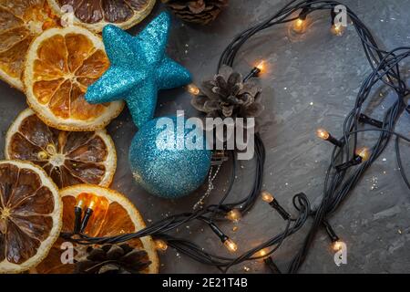 Weihnachtliche Komposition auf dunklem Beton-Hintergrund. Girlande Spielzeug und Lichter mit getrockneten Orangenscheiben. Draufsicht, selektiver Fokus. Stockfoto