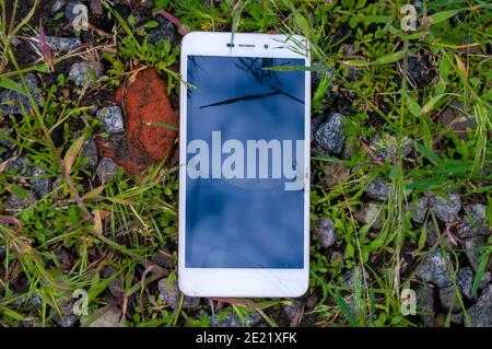 Geknackt Smartphone liegt auf Steinen mit Gras auf dem Boden. Stock Foto Stockfoto