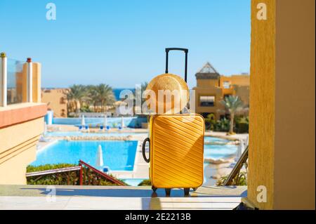 Reise, Sommerferien und Urlaubskonzept gelben Koffer mit Hut auf dem Hintergrund des Hotel-Pool-Bereich in Ägypten Stockfoto