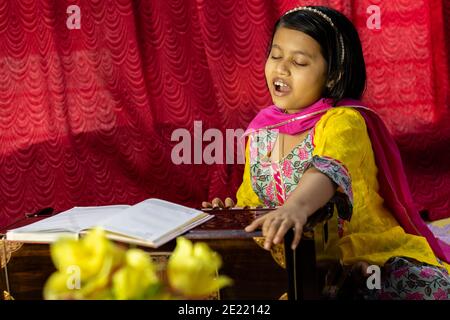 Ein indisches nettes Mädchen Kind singen und spielen Harmonium in Ethnische Kleidung Stockfoto