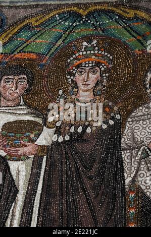 Theodora, Kaiserin des byzantinischen oder östlichen Römischen Reiches, hält einen Kommunion-Kelch, während sie mit Mitgliedern ihres Gefolges steht. Byzantinisches Mosaik in der Basilika di San Vitale in Ravenna, Emilia-Romagna, Italien. Das Mosaik wurde in den 500s v. Chr. erschaffen, ein paar Jahre nachdem Ravenna vom byzantinischen Reich aus den Ostrogoten gefangen wurde. Stockfoto