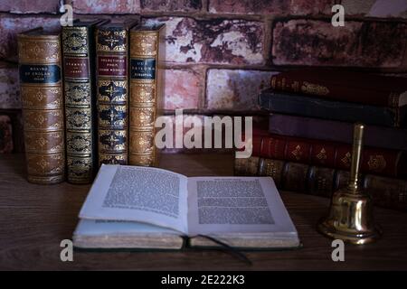 Klassische Stilllebensszene aus ledergebundenen Büchern, einem offenen Buch und einer Messingglocke. Stockfoto