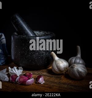 Schwarzer Granitmörtel und Mörser mit frischen Knoblauchzwiebeln. Stockfoto