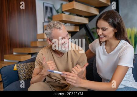 Junge dunkelhaarige Frau zeigt ihm ihren positiven Schwangerschaftstest Rehemann Stockfoto