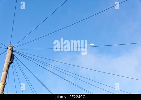 Netzwerk-Kommunikationskabel auf Strommast gegen blauen Himmel mit Eine Ebene im Hintergrund Stockfoto