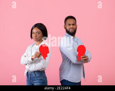 Unglücklicher schwarzer Mann und Frau, die Hälften des gebrochenen Herzens halten Auf pinkem Studiohintergrund Stockfoto