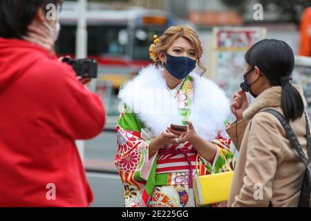 Eine Frau mit Kimono und Maske spricht mit der Presse am Shibuya Crossing während des "Coming of Age"-Tages Tokyo.Coming des Age Day feiert diejenigen, die 20 Jahre alt geworden sind. Es ist Feiertag am zweiten Montag im Januar in Japan. Angesichts der steigenden COVID19-Infektionsrate in ganz Japan war der Coming of Age Day von 2021 jedoch nicht wie gewöhnlich. Die feierliche Zeremonie war nur online in den meisten Büros der Stadt in Japan. Im beliebten Ort Shibuya Crossing waren nur wenige Mädchen in schönen Kimono. Alle Menschen tragen Maske. Stockfoto