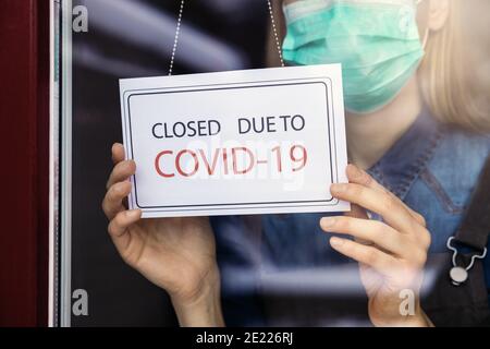 Inhaber eines kleinen Unternehmens mit Gesichtsmaske, die ein geschlossenes Schild aufmacht Schaufenster wegen Covid-19 Stockfoto