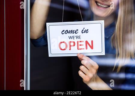 Lächelnde Frau, die an einem kleinen örtlichen Geschäft ein Schild aufgehängt hat Türfenster Stockfoto