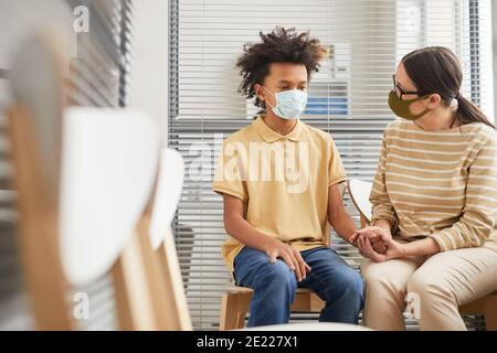 Porträt der fürsorglichen Mutter tröstenden Sohn während in der Warteschlange in der medizinischen Klinik für die Impfung, beide mit Masken, Kopierer Raum Stockfoto