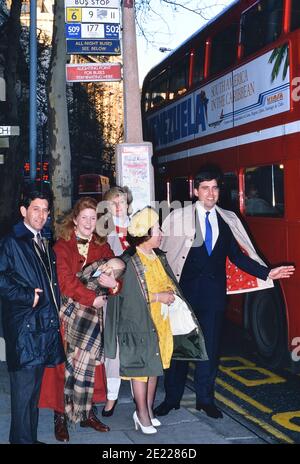 Eine Gruppe von Imitatoren der britischen Königsfamilie, die an einer Bushaltestelle anstehen, um einen roten Doppeldeckerbus zu nehmen. London. England, Großbritannien, um 1989 Stockfoto