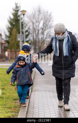 POZNAN, POLEN - 25. Dezember 2020: Erwachsene Frau mit Gesichtsmaske und warmen Kleidern, die an einem kalten Wintertag mit Kindern auf einem Bürgersteig in der Stadt spazieren geht. Stockfoto