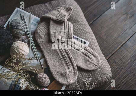 Ein Paar von Hand gestrickte Socken mit Garn Ball und Stricknadeln. Natürliche Farben. Dunkler rustikaler Holzhintergrund. Stockfoto