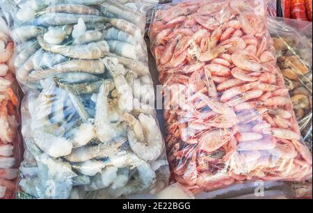 Zwei große Plastiktüten mit gefrorenen rohen und gekochten Garnelen, auf der Theke des Fischmarktes. Stockfoto