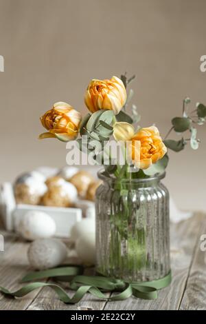 Ein Blumenstrauß in einer Glasvase mit dekorativen Elementen auf verschwommenem Hintergrund. Osterfeiertagskonzept. Stockfoto