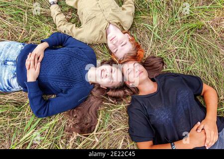 Sommerferien Urlaub glückliche Menschen Konzept. Draufsicht Gruppe von drei Freunden, die im Kreis auf Gras liegen, lächeln und zusammen im Freien Spaß haben. Picn Stockfoto