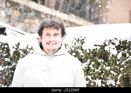 Porträt eines lächelnden Mannes im Hoodie, der neben verschneiten Büschen liegt. Gekleidet in eine weiße Jacke, braune Haare mit grauen Haaren. Schneetag in Munilla, La Rioja. Te Stockfoto