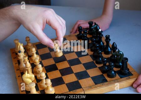 Brettspiel zu Hause. Ein Kind spielt alleine Schach. Altes Holzschachbrett. Kinderhände. Schachfiguren auf einem Schachbrett. Stockfoto