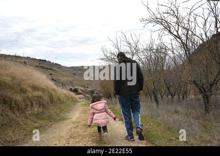 Fünfjähriges Mädchen, das mit ihrem Vater auf einer Landstraße läuft. Im Winter in warme Kleidung gekleidet. Stockfoto