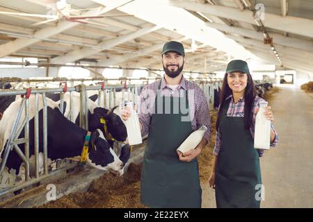 Ein paar junge Bauern halten Glasflaschen mit frischer, köstlicher Bio-Milch auf dem Bauernhof. Stockfoto