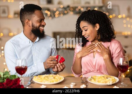 Lächelnder schwarzer Mann macht Vorschlag mit Ring zu seinem Verlobten Stockfoto