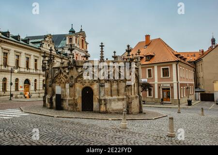 Steinbrunnen im historischen Stadtzentrum mit Kopfsteinpflasterstraße, bunten Fassaden, Kutna Hora, Tschechische Republik.UNESCO-Weltkulturerbe. Stockfoto