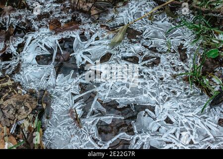Abstrakter Winterhintergrund, rissige Eis auf gefrorener Pfütze. Eisfragmente auf gefrorenem Wasser. Das Eis zerbrochene Stücke.Eis auf einer gefrorenen Wasserpfütze im Winter Stockfoto