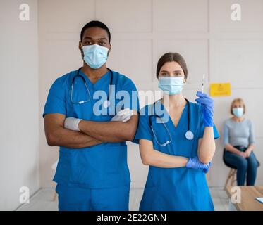 Porträt von Ärzten in medizinischen Masken und Uniformen halten Spritze Mit Covid-19-Impfstoff im Gesundheitszentrum Stockfoto