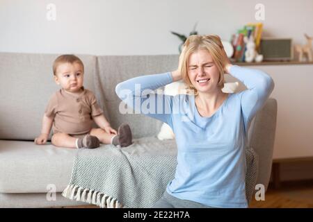 Gestresste Mutter leidet unter Kopfschmerzen, sitzen mit Baby zu Hause Stockfoto