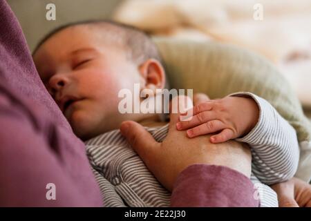 Ein kleiner Junge schläft auf dem Schoß seiner Mutter Legen Sie ihre Hand auf seinen Bauch Stockfoto