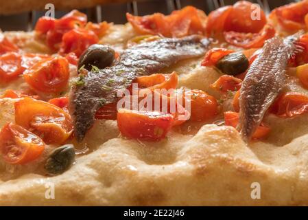 Nahaufnahme von in Scheiben geschnittenen Kirschtomaten auf Pizza gekocht mit Sardellenfilets Stockfoto