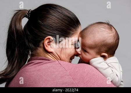 Eine Mutter hält ihren neugeborenen Jungen und schaut zu Er mit Liebe und Lächeln Stockfoto