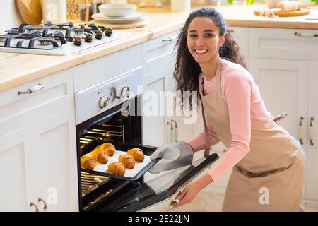 Glückliche Junge Frau, Die Tablett Mit Frisch Gebackenen Croissants Herausnimmt Aus Dem Ofen Stockfoto