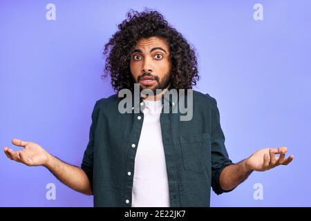 Emotionales arabisches Männchen ist Missverständnis, reagiert auf etwas, spreizt Arme, gestikiert. Isolierter violetter Hintergrund Stockfoto