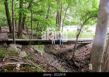 Zwei Mädchen sitzen zusammen und ruhen auf Brücke im Wald Beim Wandern Stockfoto