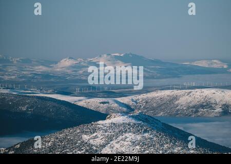 Windmühlen gegen schneebedeckte Berggipfel an einem klaren blauen Himmel Tag, Sierra de Guadarrama, Madrid Stockfoto