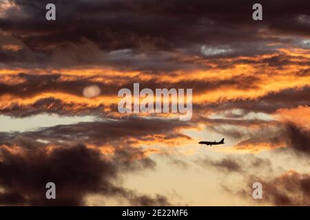 Ein kommerzielles Flugzeug steigt bei Sonnenuntergang durch Wolken ab. Stockfoto