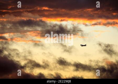 Ein kommerzielles Flugzeug steigt bei Sonnenuntergang durch Wolken ab. Stockfoto