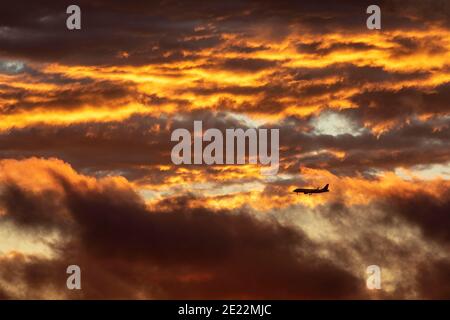 Ein kommerzielles Flugzeug steigt bei Sonnenuntergang durch Wolken ab. Stockfoto